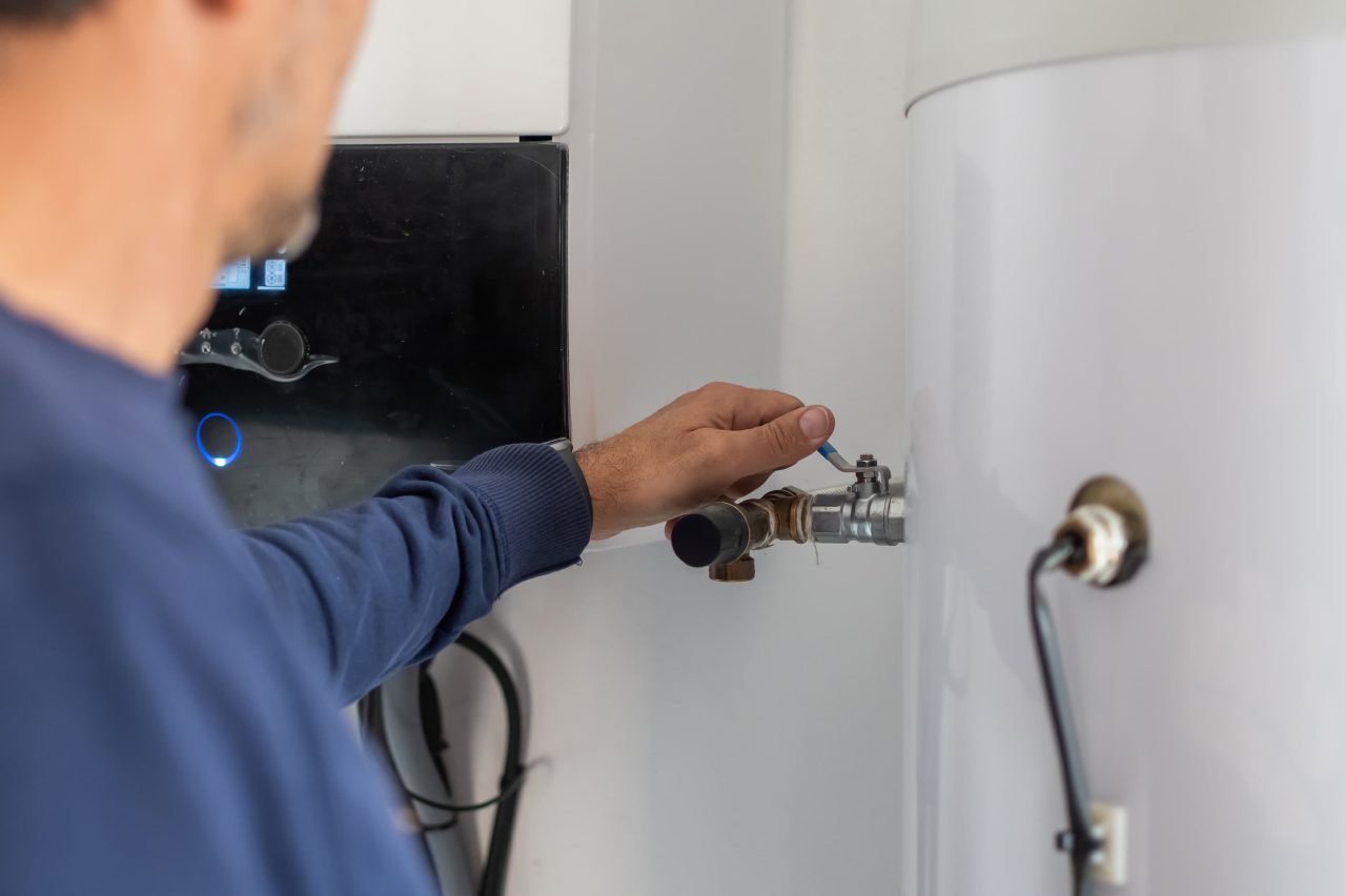 A man's hand turning a valve on a boiler
